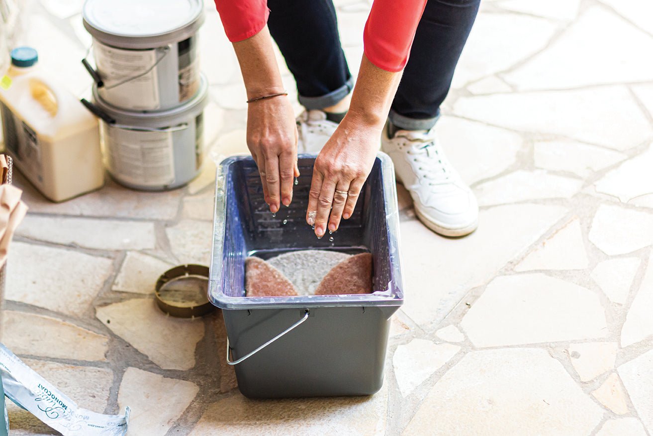 Person using Rubio Monocoat cleaning tools and a bucket on a tiled floor.