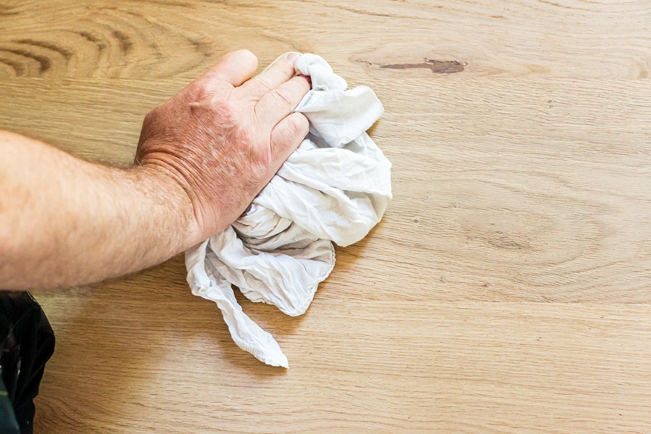 Hand using a white cloth to wipe a wooden surface.
