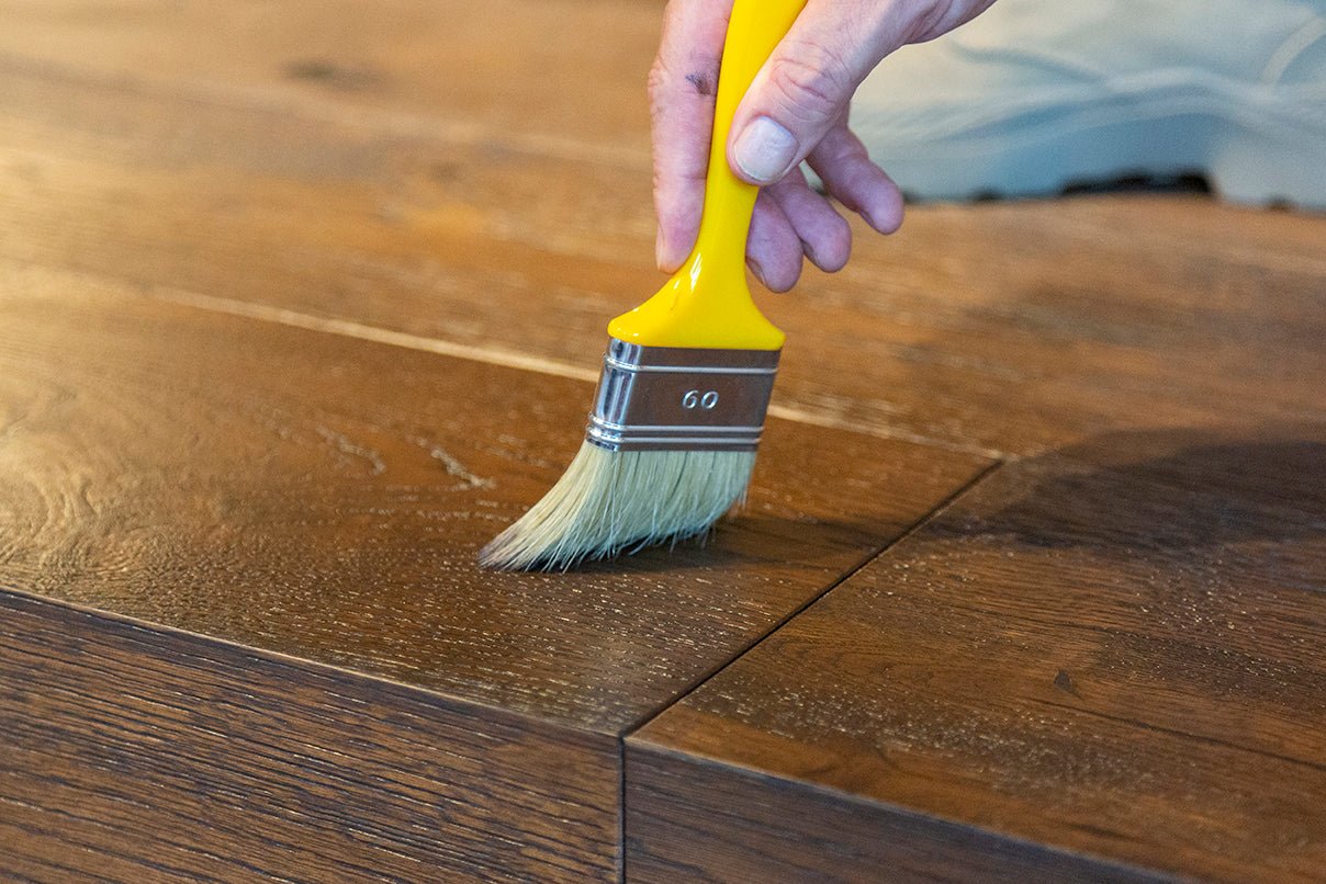 Person applying Rubio Monocoat wood finish to a wooden surface using a yellow brush.